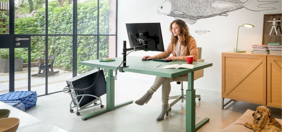 Modern home workspace with a green sit-stand desk, ergonomic monitor arm, and a cable management system for a tidy desk.